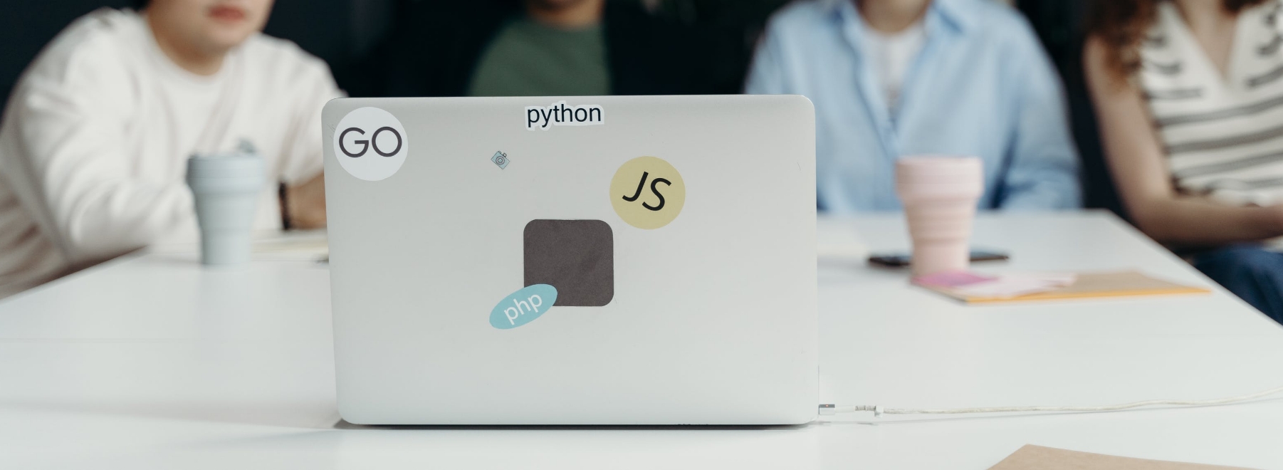 Photo of a laptop in the foreground with people in the background.