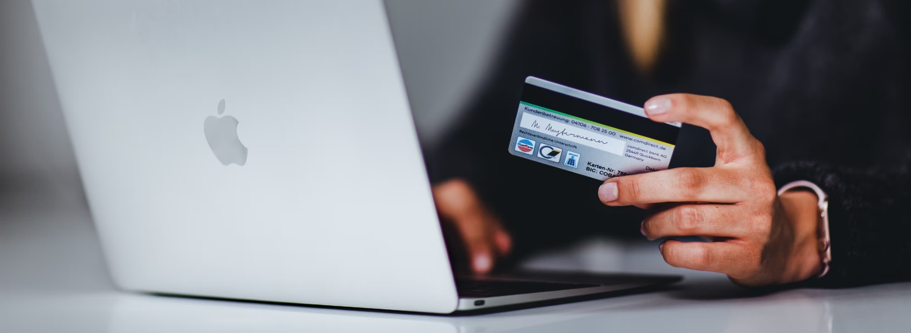 A person in front of a laptop, holding a credit card.